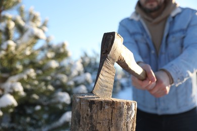 Man chopping wood with axe outdoors on winter day, closeup. Space for text