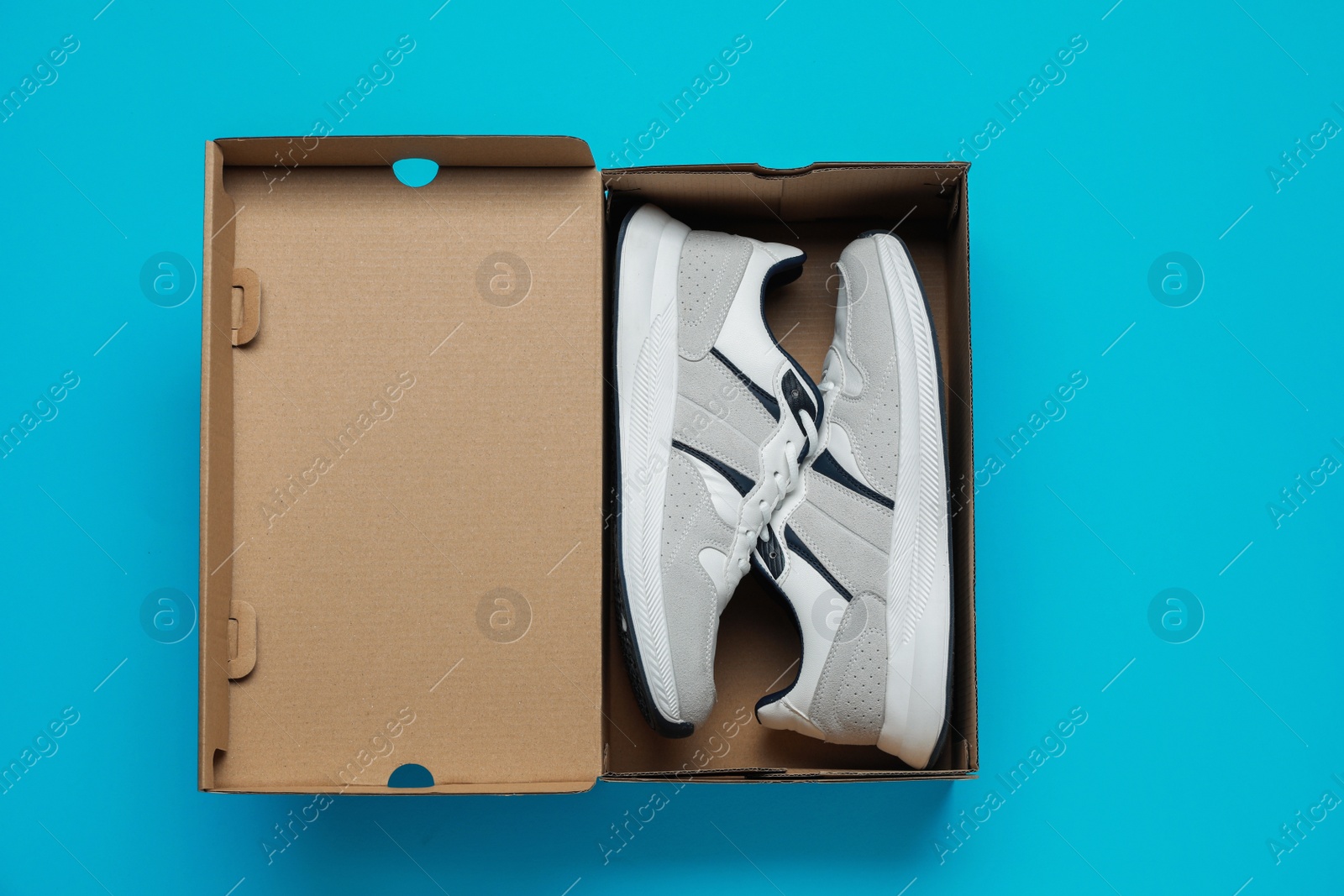 Photo of Comfortable sports shoes in cardboard box on light blue background, top view