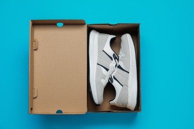 Photo of Comfortable sports shoes in cardboard box on light blue background, top view