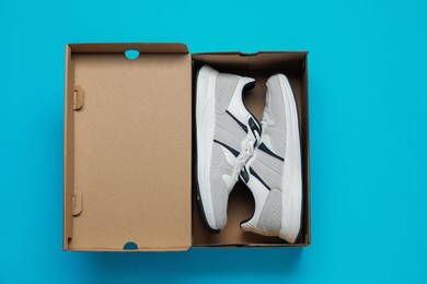 Comfortable sports shoes in cardboard box on light blue background, top view