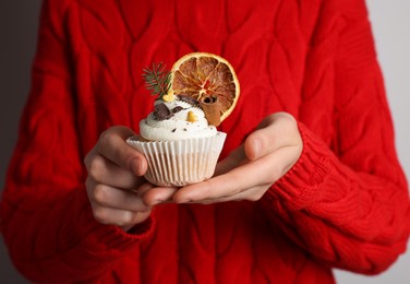 Woman holding tasty Christmas cupcake with cream and decor on light background, closeup