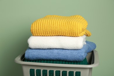 Photo of Plastic laundry basket with clean clothes near light green wall, closeup