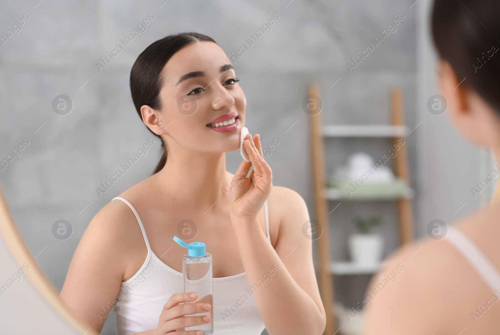 Photo of Beautiful woman removing makeup with cotton pad near mirror indoors