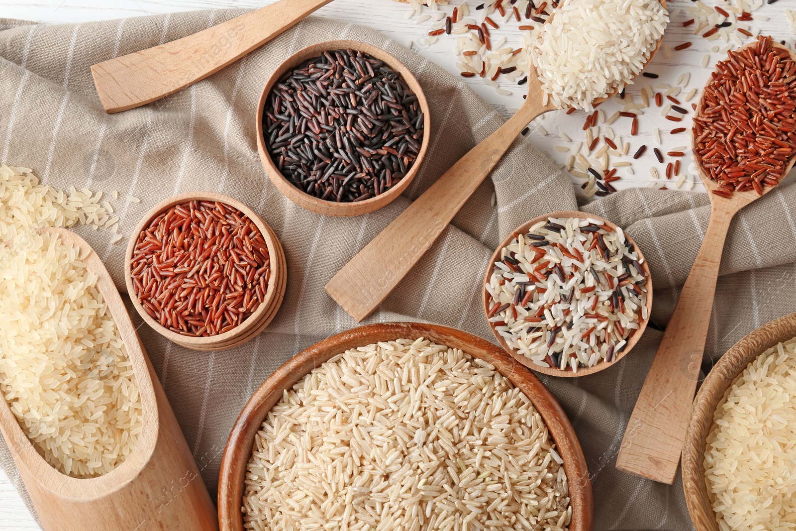 Photo of Flat lay composition with brown and other types of rice on wooden background