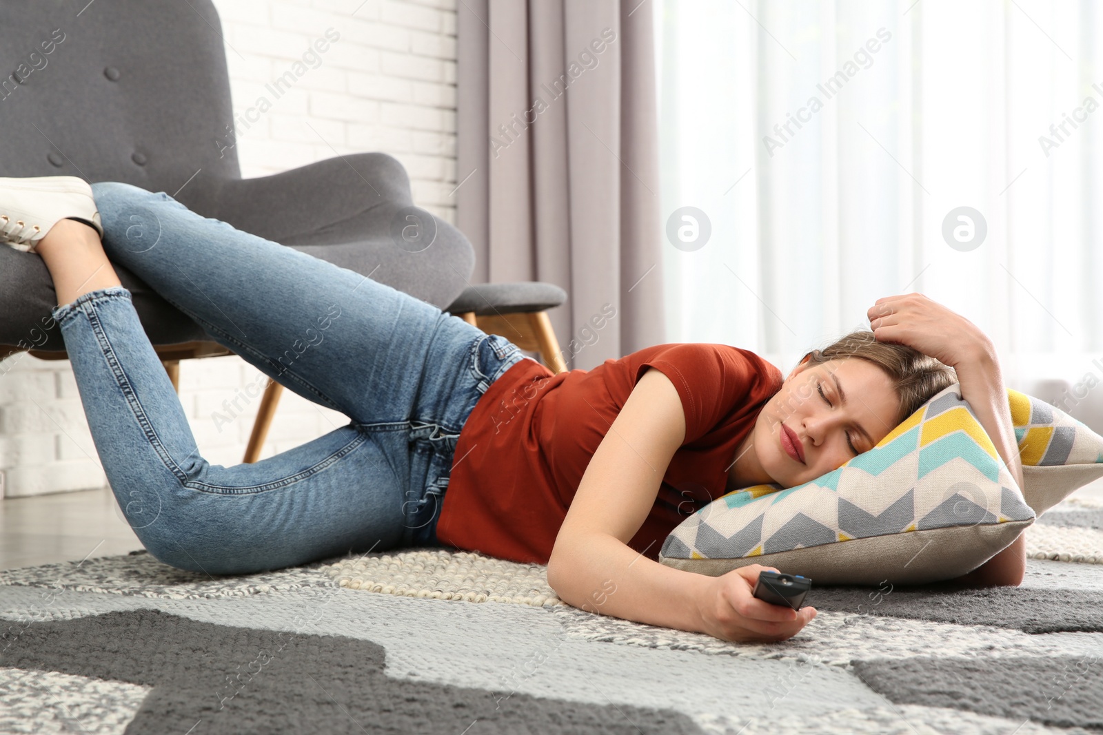 Photo of Lazy young woman with TV remote sleeping on floor at home