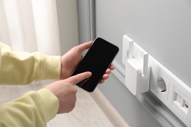 Woman using smartphone for wireless Wi-Fi repeater indoors, closeup