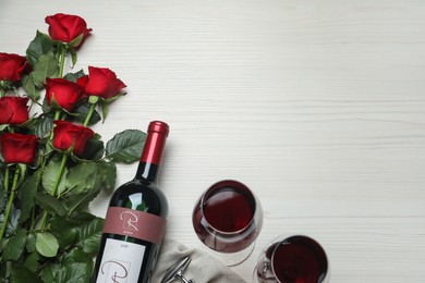 Bottle and glasses of red wine with beautiful roses on white wooden table, flat lay. Space for text