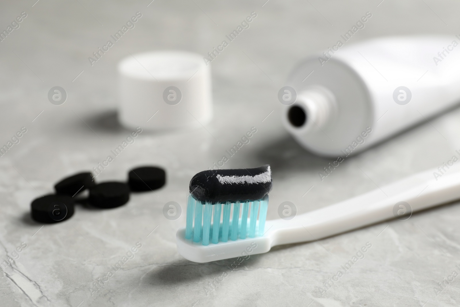 Photo of Brush with charcoal toothpaste on light grey table, closeup