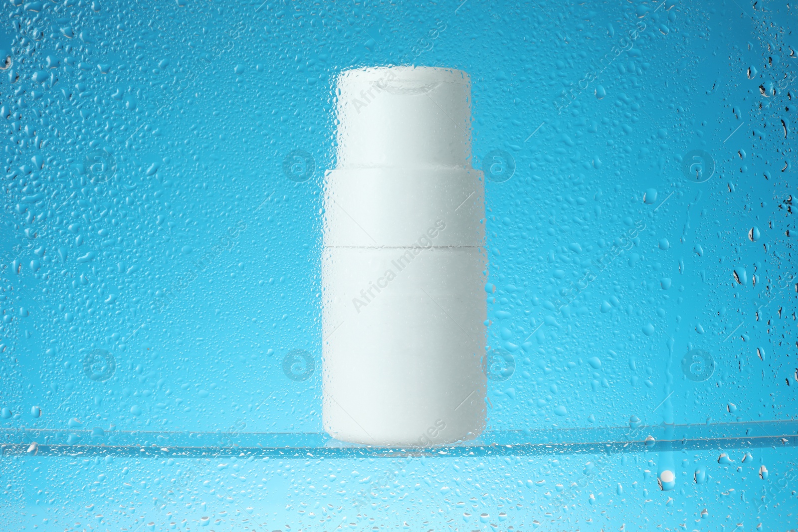 Photo of Bottle with moisturizing cream on light blue background, view through wet glass