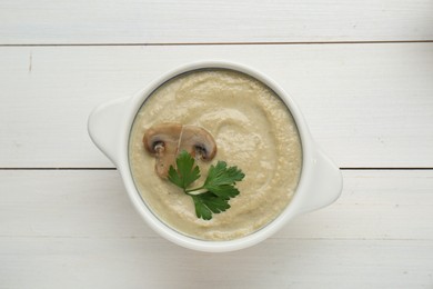 Delicious mushroom cream soup with parsley on white wooden table, top view
