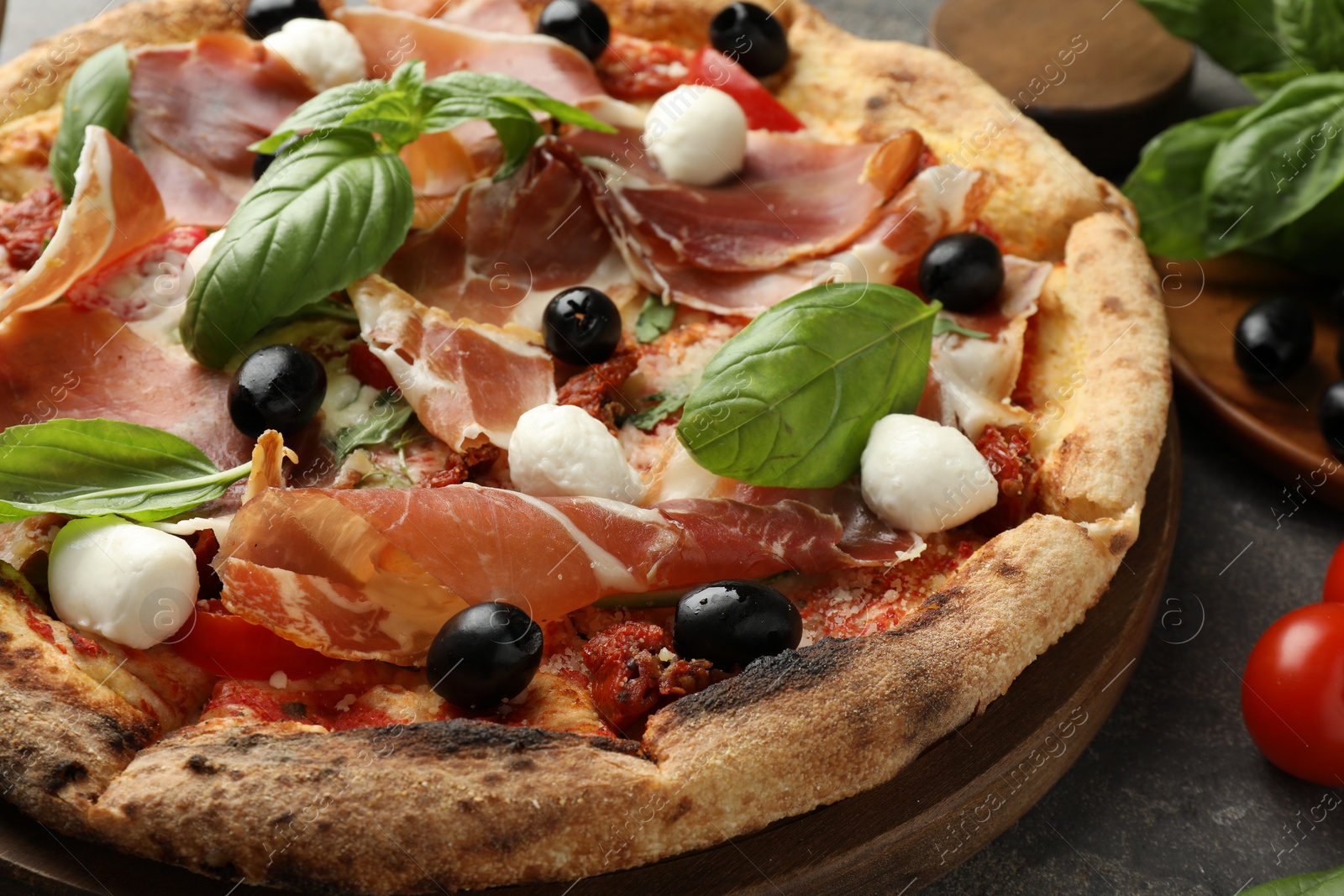 Photo of Tasty pizza with cured ham, olives, mozzarella cheese, sun-dried tomato and arugula on table, closeup