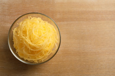 Photo of Bowl of cooked spaghetti squash on wooden table, top view with space for text