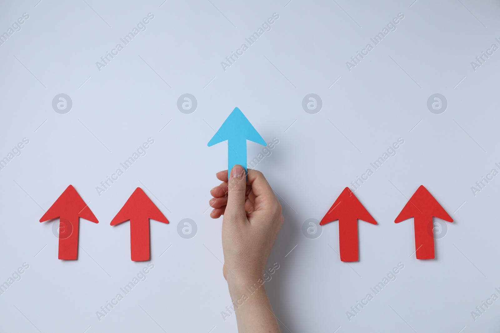 Photo of Woman holding light blue paper arrow among red arrows on white background, top view. Space for text