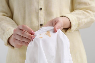 Woman holding shirt with stain against light background, closeup