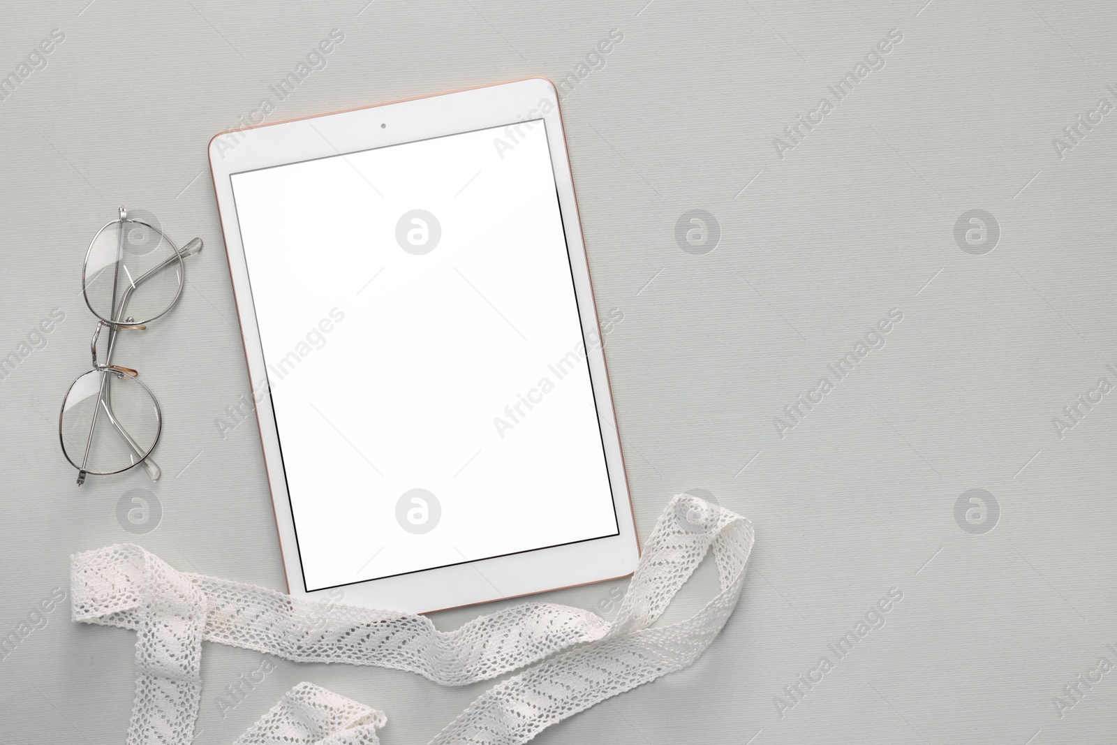 Photo of Modern tablet, glasses and ribbon on light grey background, flat lay. Space for text