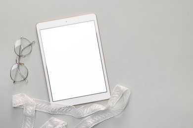 Photo of Modern tablet, glasses and ribbon on light grey background, flat lay. Space for text