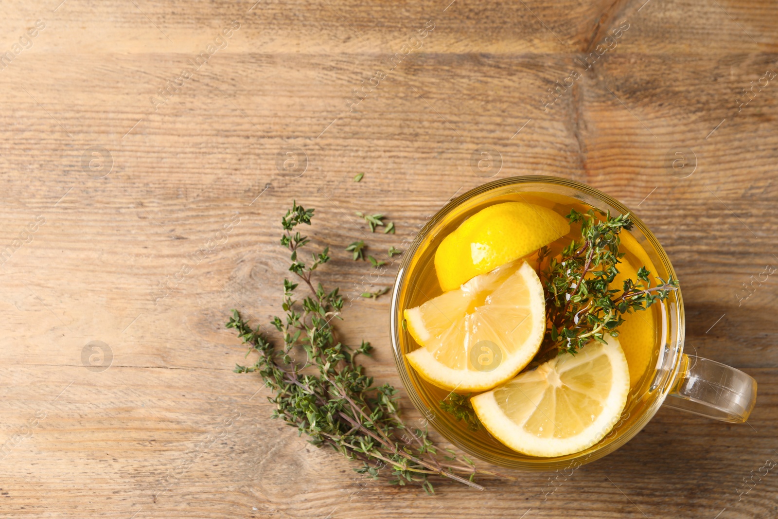 Photo of Fresh thyme tea with pieces of lemon on wooden table, flat lay. Space for text