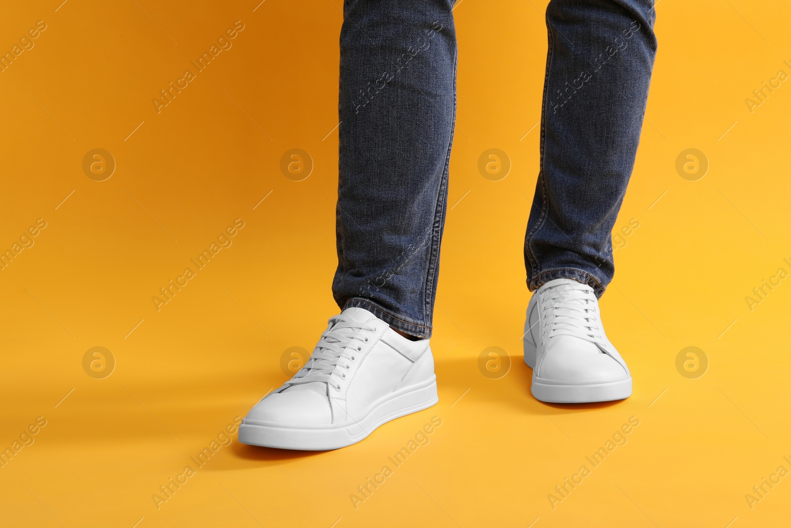 Photo of Man wearing stylish white sneakers on yellow background, closeup