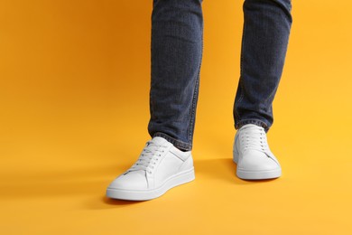 Man wearing stylish white sneakers on yellow background, closeup