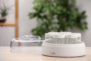 Modern yogurt maker with empty jars on table indoors. Space for text