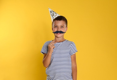 Photo of Little boy with photo booth props on yellow background. Birthday celebration