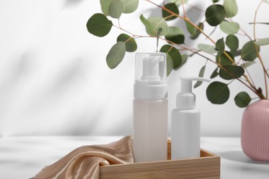 Photo of Bottles of face cleansing products and eucalyptus branches on table