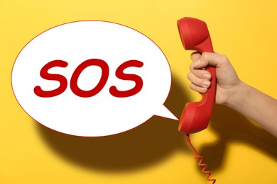 Image of Woman holding telephone handset on yellow background, closeup. Emergency SOS call