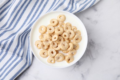 Breakfast cereal. Tasty corn rings with milk in bowl on white marble table, top view