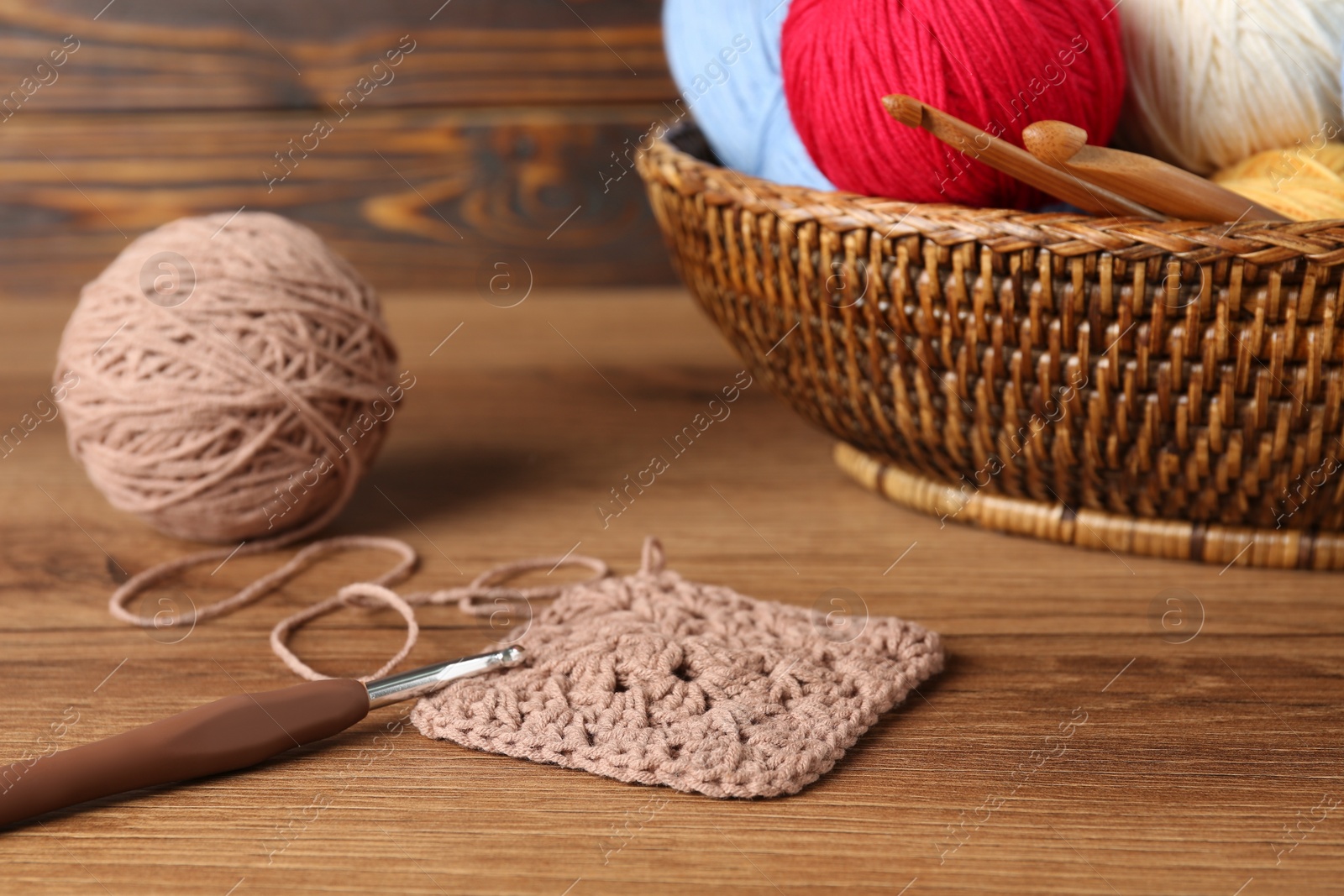 Photo of Clews, knitting and crochet hooks on wooden table, closeup