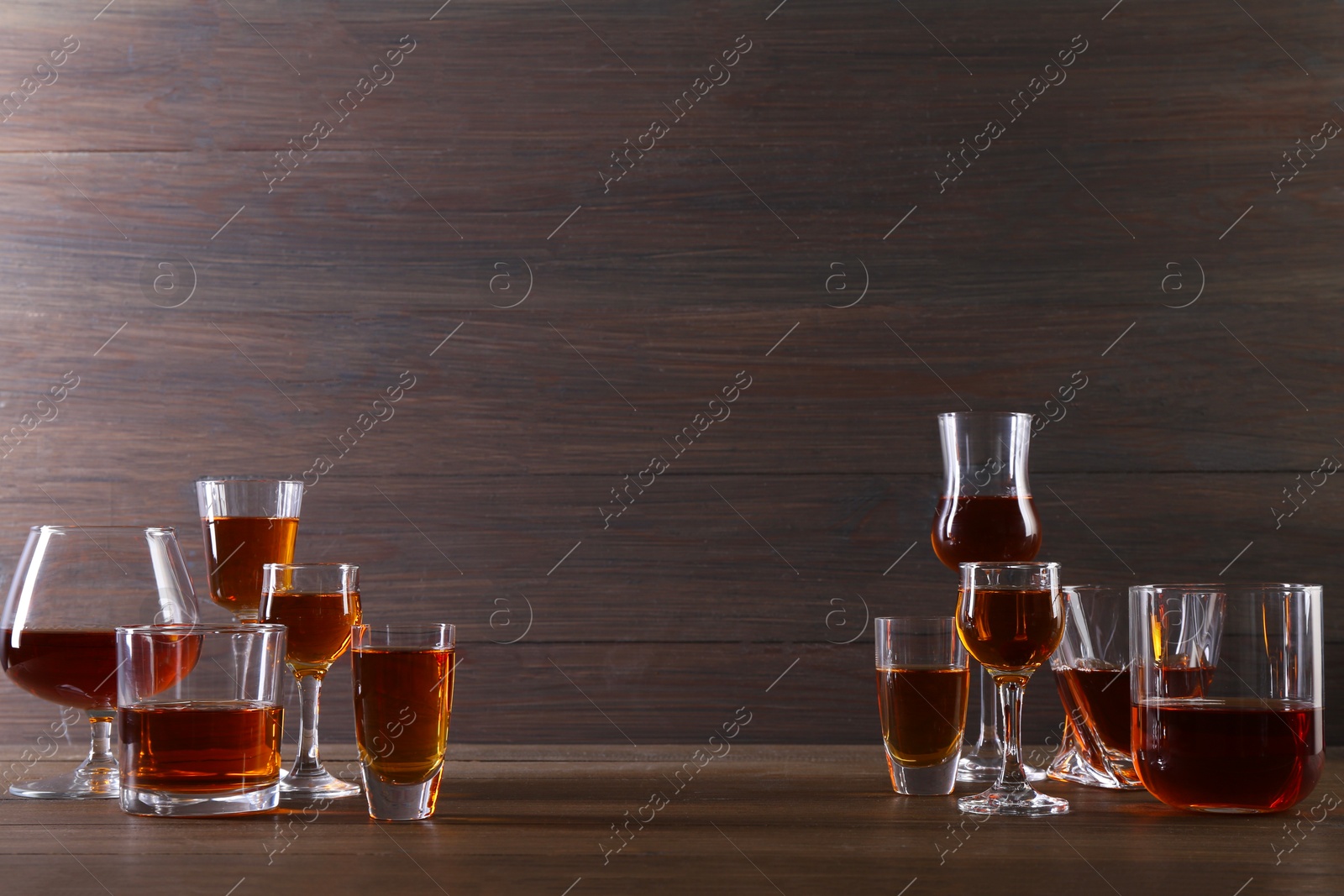 Photo of Different delicious liqueurs in glasses on wooden table, space for text