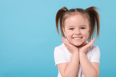 Portrait of happy little girl on light blue background, space for text