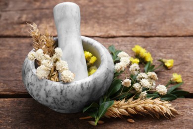 Photo of Mortar with pestle, dry flowers and ears of wheat on wooden table