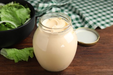 Photo of Jar of delicious mayonnaise and fresh salad on wooden table