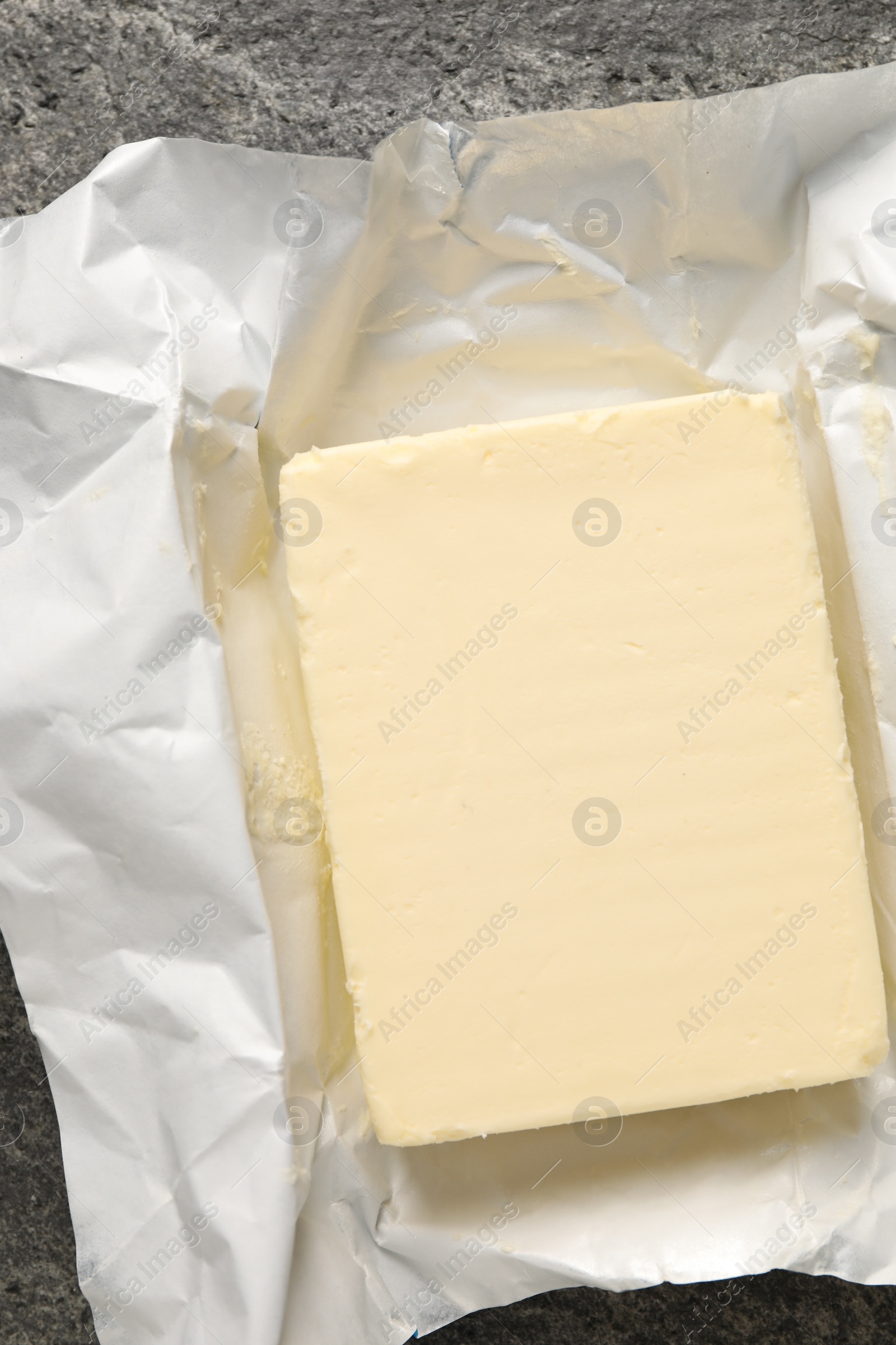 Photo of Block of tasty butter in open foil packaging on grey table