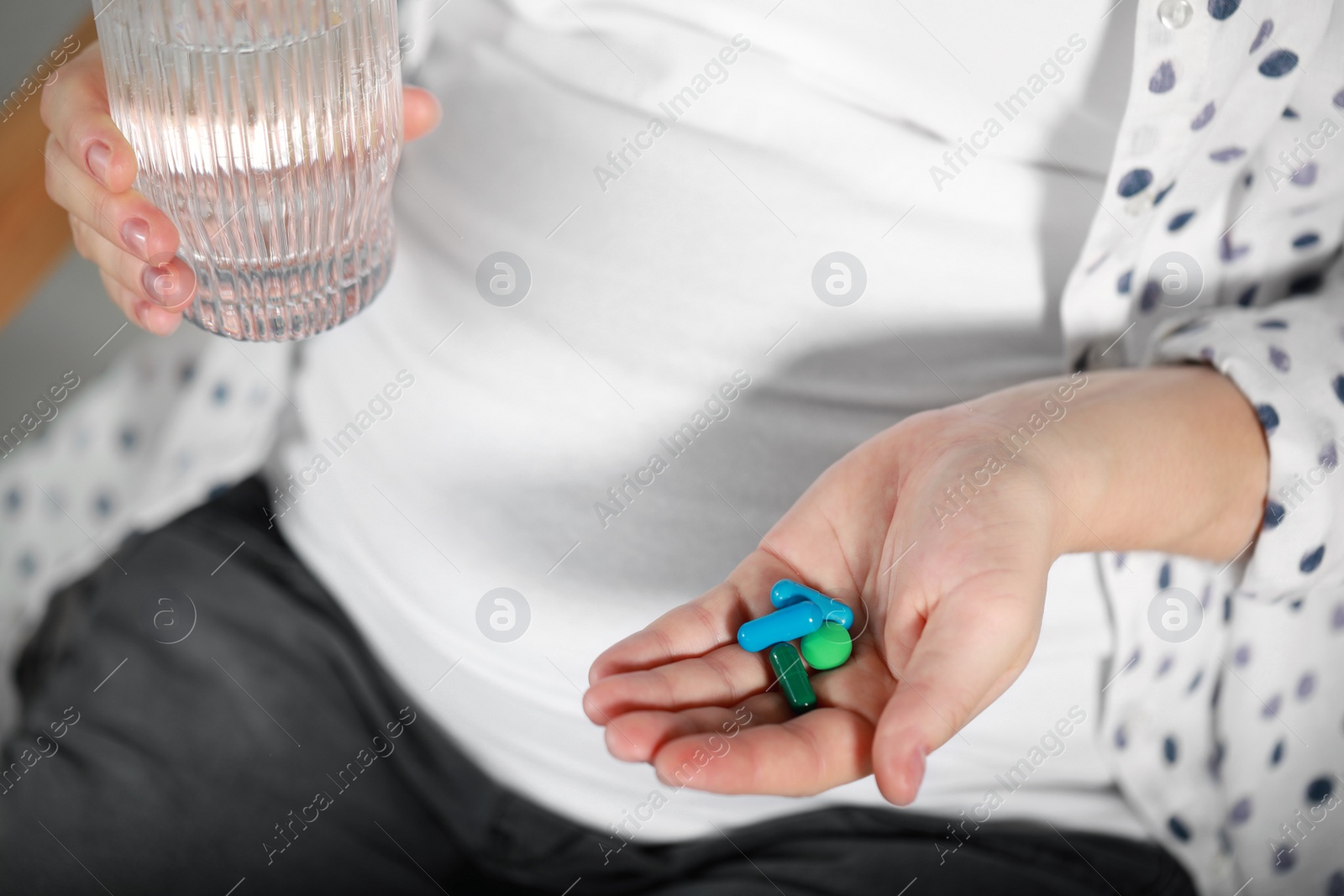 Photo of Pregnant woman holding pile of pills and glass with water, closeup