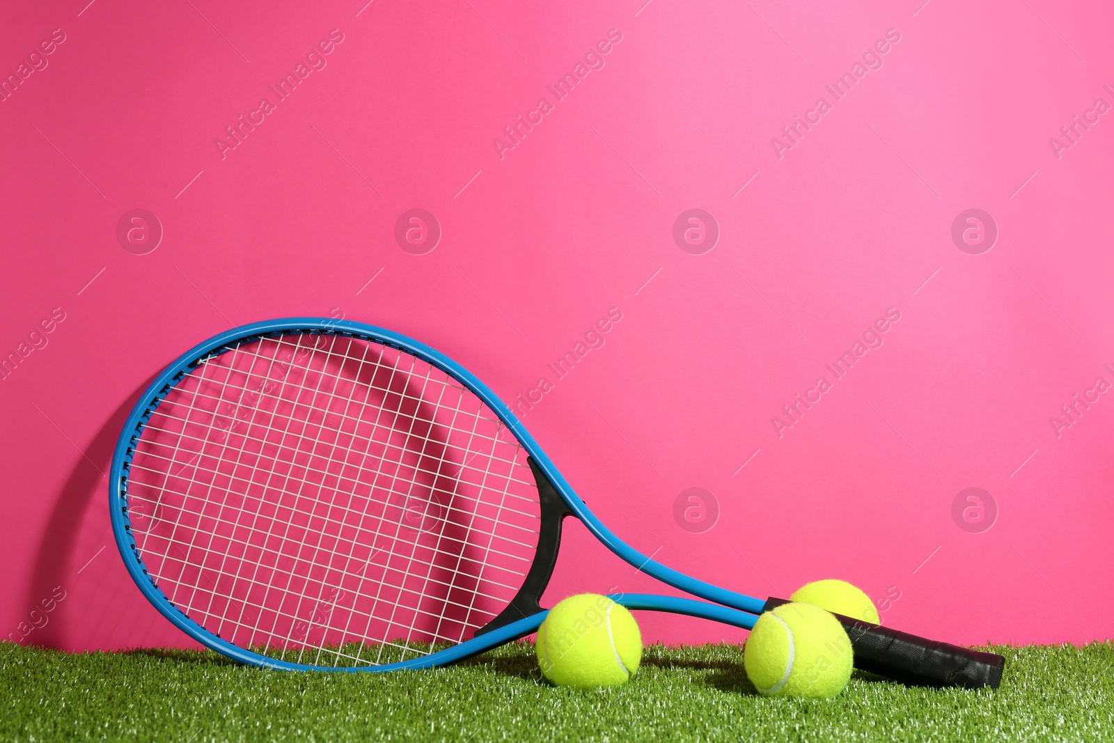 Photo of Tennis racket and balls on green grass against pink background. Space for text