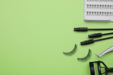 Photo of Flat lay composition with fake eyelashes, brushes and tools on green background. Space for text