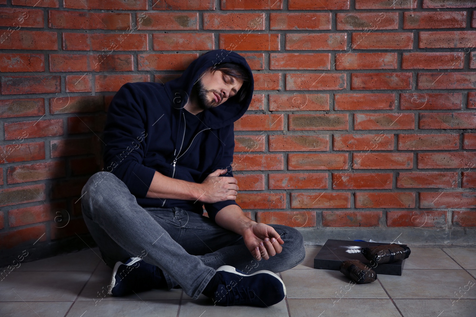 Photo of Young addicted man sitting near brick wall after using drugs. Space for text