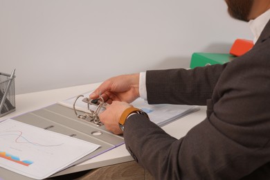 Businessman putting document into file folder at white table in 'office, closeup