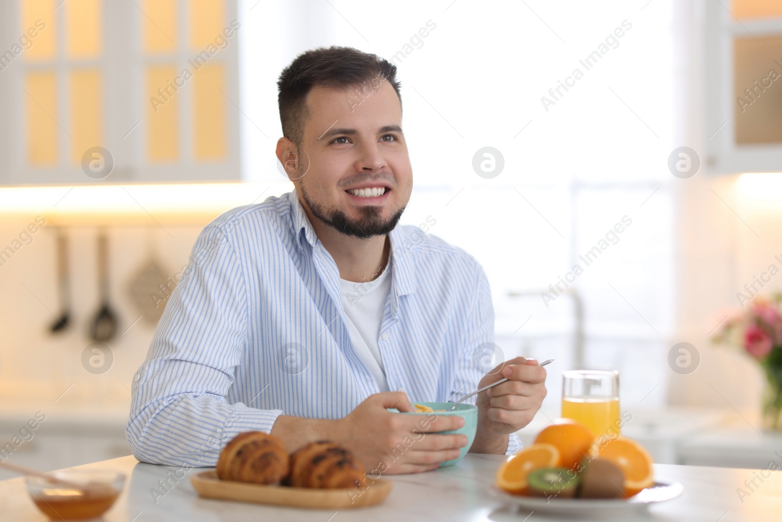 Photo of Smiling man eating tasty cornflakes at breakfast indoors