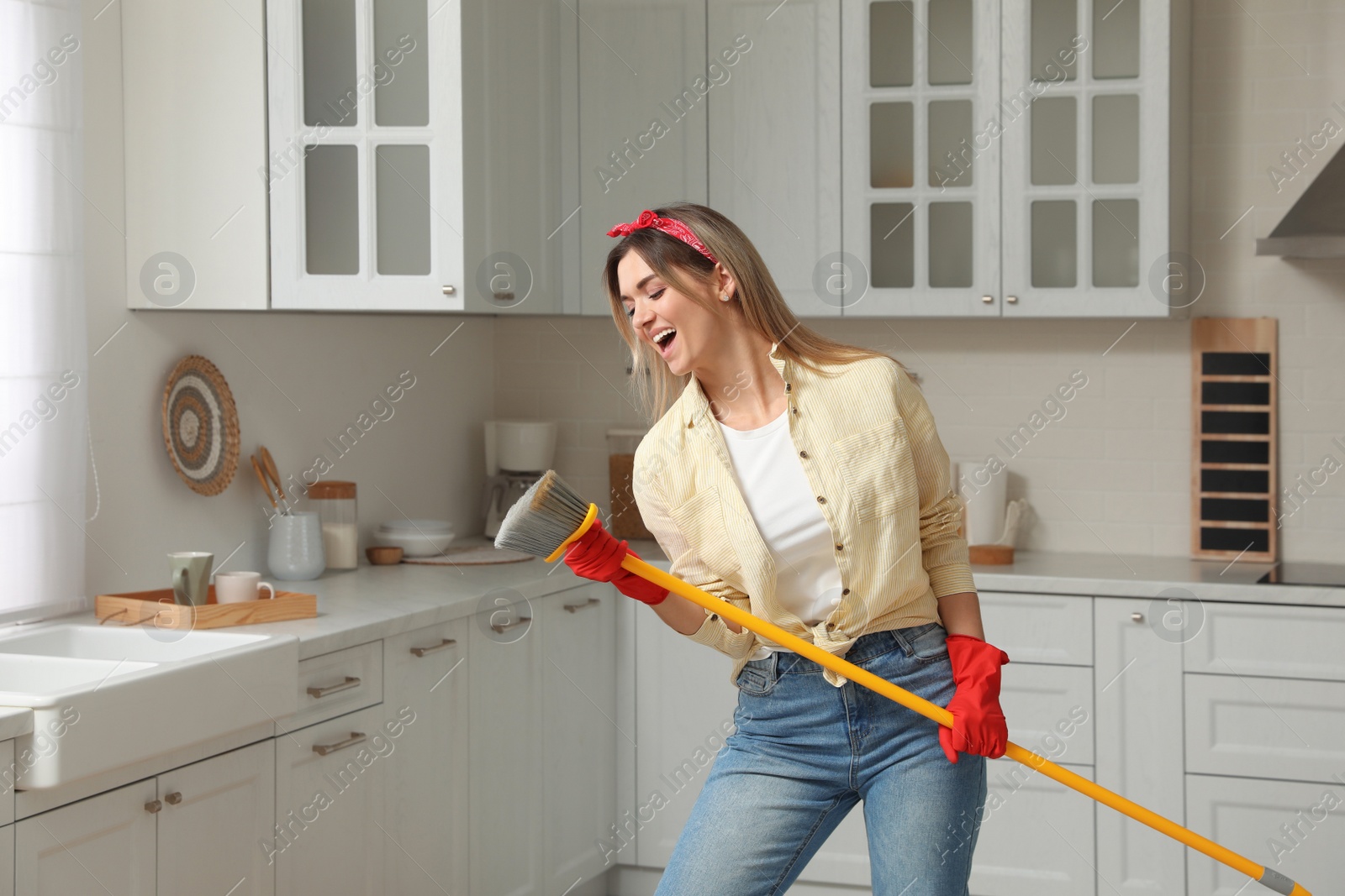 Photo of Woman with broom singing while cleaning in kitchen