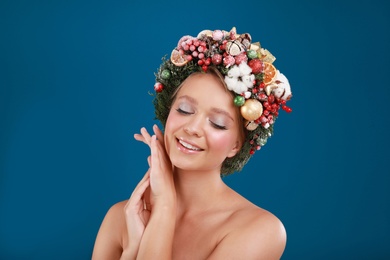 Beautiful young woman wearing Christmas wreath on blue background