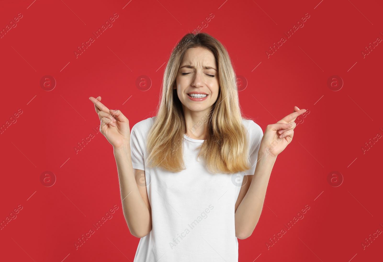 Photo of Woman with crossed fingers on red background. Superstition concept