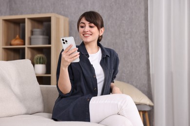 Photo of Beautiful young housewife using smartphone on sofa at home