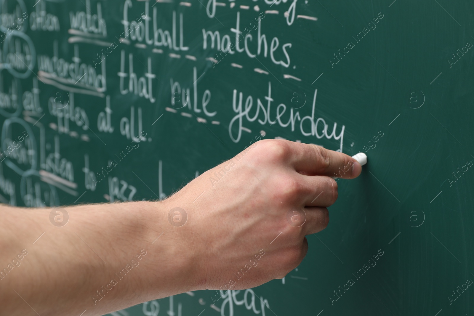 Photo of English teacher writing with chalk on green chalkboard, closeup