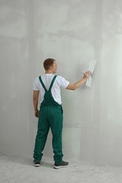 Professional worker plastering wall with putty knife indoors