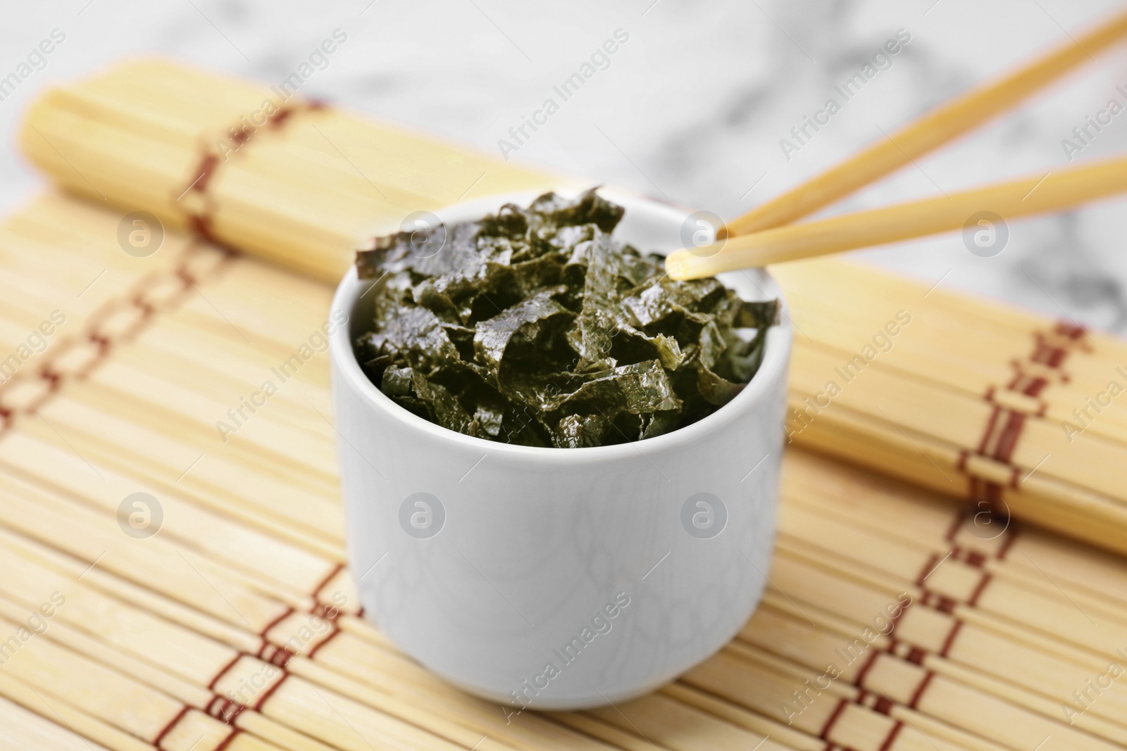 Photo of Chopped nori sheets with chopsticks on white marble table, closeup