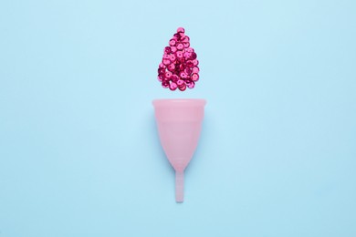 Menstrual cup near drop made of pink sequins on light blue background, flat lay