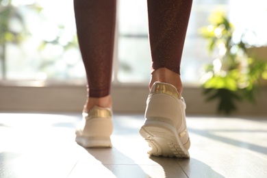 Photo of Young woman wearing stylish sneakers indoors, closeup