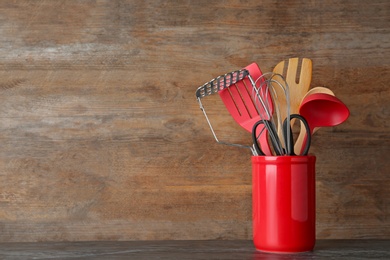 Photo of Holder with kitchen utensils on table against wooden background. Space for text